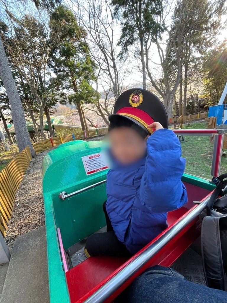 移動遊園地のミニ機関車に乗り制帽をかぶる子ども
