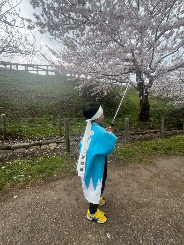 新選組の衣装で刀を構える子ども、満開の桜を背景に