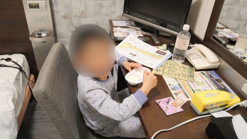 コンフォートホテル函館の客室デスクで過ごす子ども、周りに観光マップやパンフレット