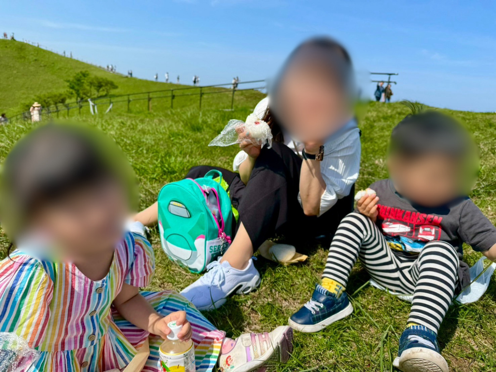 大室山山頂の芝生でおにぎりを食べる親子